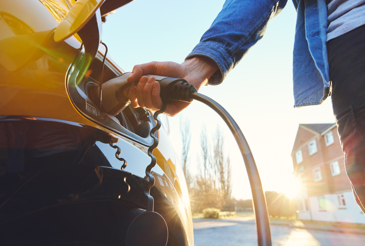 Man with his hand on an electric vehicle charger charging his car